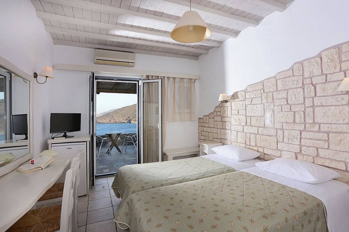 Une chambre avec deux lits, un bureau avec une télévision et un mur en pierre.