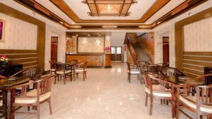 A hotel lobby with a reception desk, wooden chairs, a staircase, and a tiled floor. - Puri Nusa Indah (Denpasar)