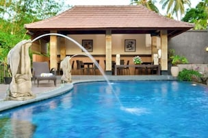 A pool with a water feature, a covered seating area, and statues.