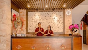 A reception desk with a carved wall backdrop, a clock, and a reception sign. - Puri Nusa Indah (Denpasar)