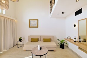 A modern living room with a sofa, a small table, a mirror, and a potted plant. - Inea Studio (Chania)