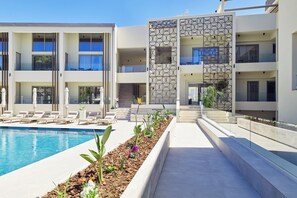 A modern hotel with a swimming pool, sun loungers, and a landscaped garden area. - Inea Studio (Chania)