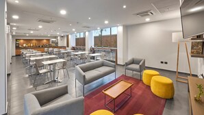 A modern dining area with tables and chairs, a sofa, and a television. - City Express by Marriott Tijuana Otay (Tijuana)