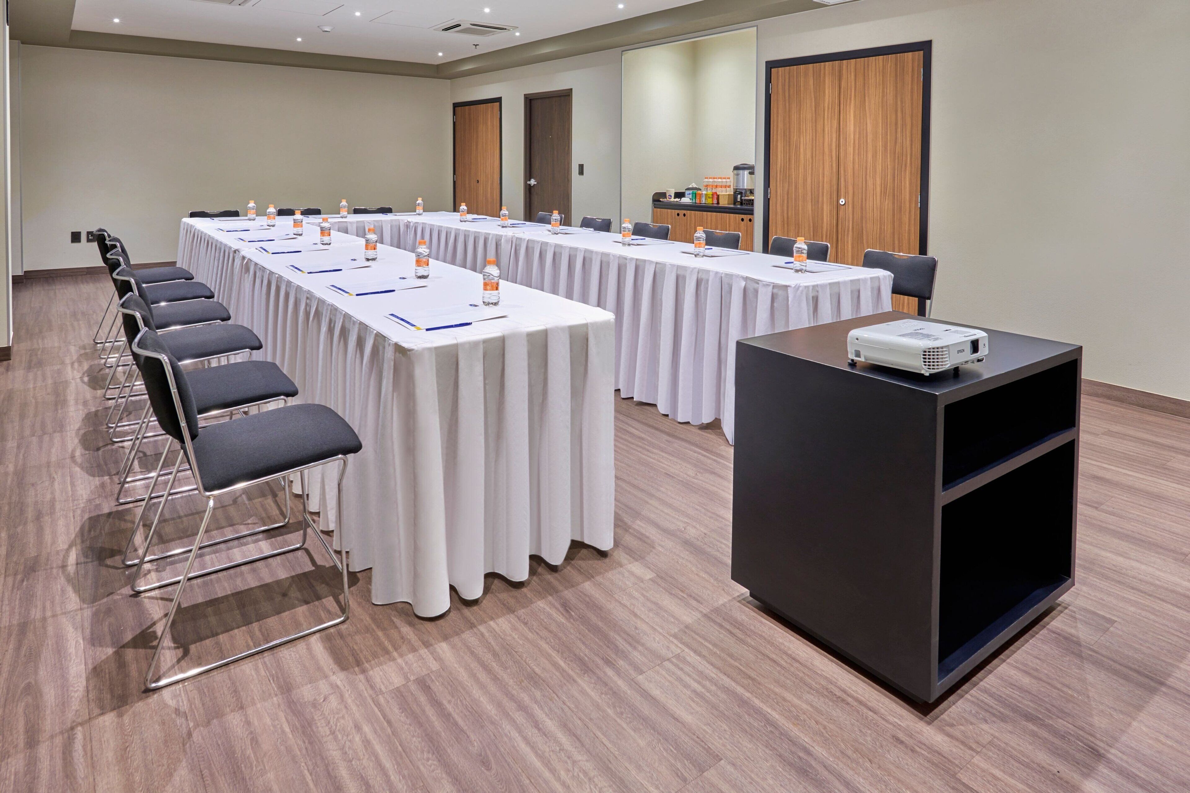 Une salle de conférence équipée de longues tables, de chaises, d’un projecteur et d’un coin café.
