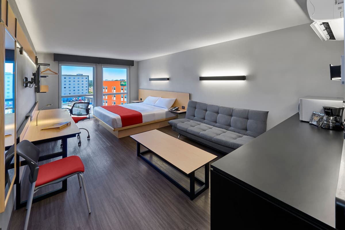 A modern hotel room with a bed, sofa, desk, and chair.