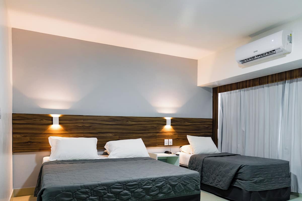 Una habitación de hotel con cama, mesitas de noche y un equipo de aire acondicionado.