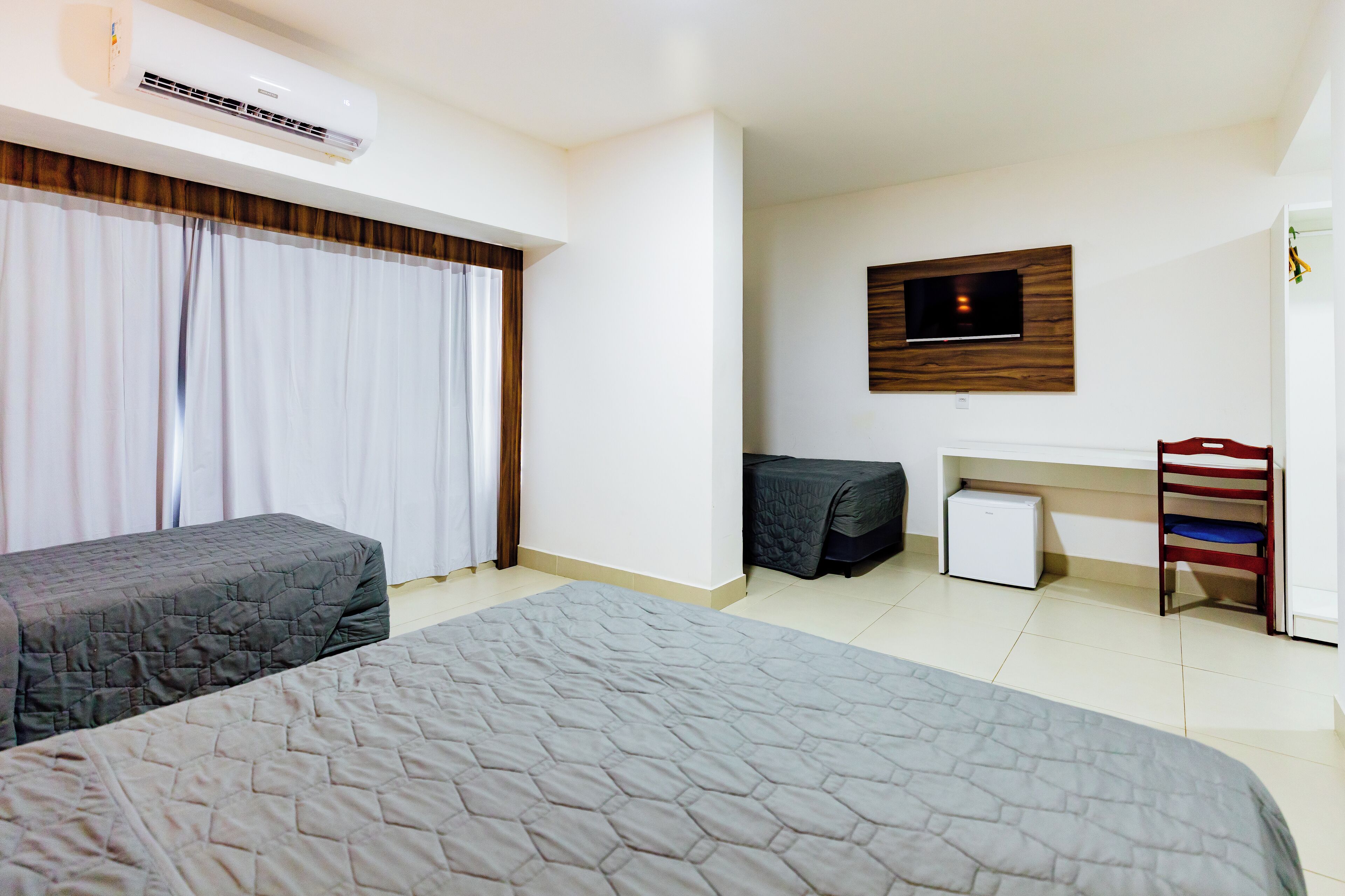 A hotel room with two beds, a TV on the wall, a desk with a chair, and a small refrigerator.