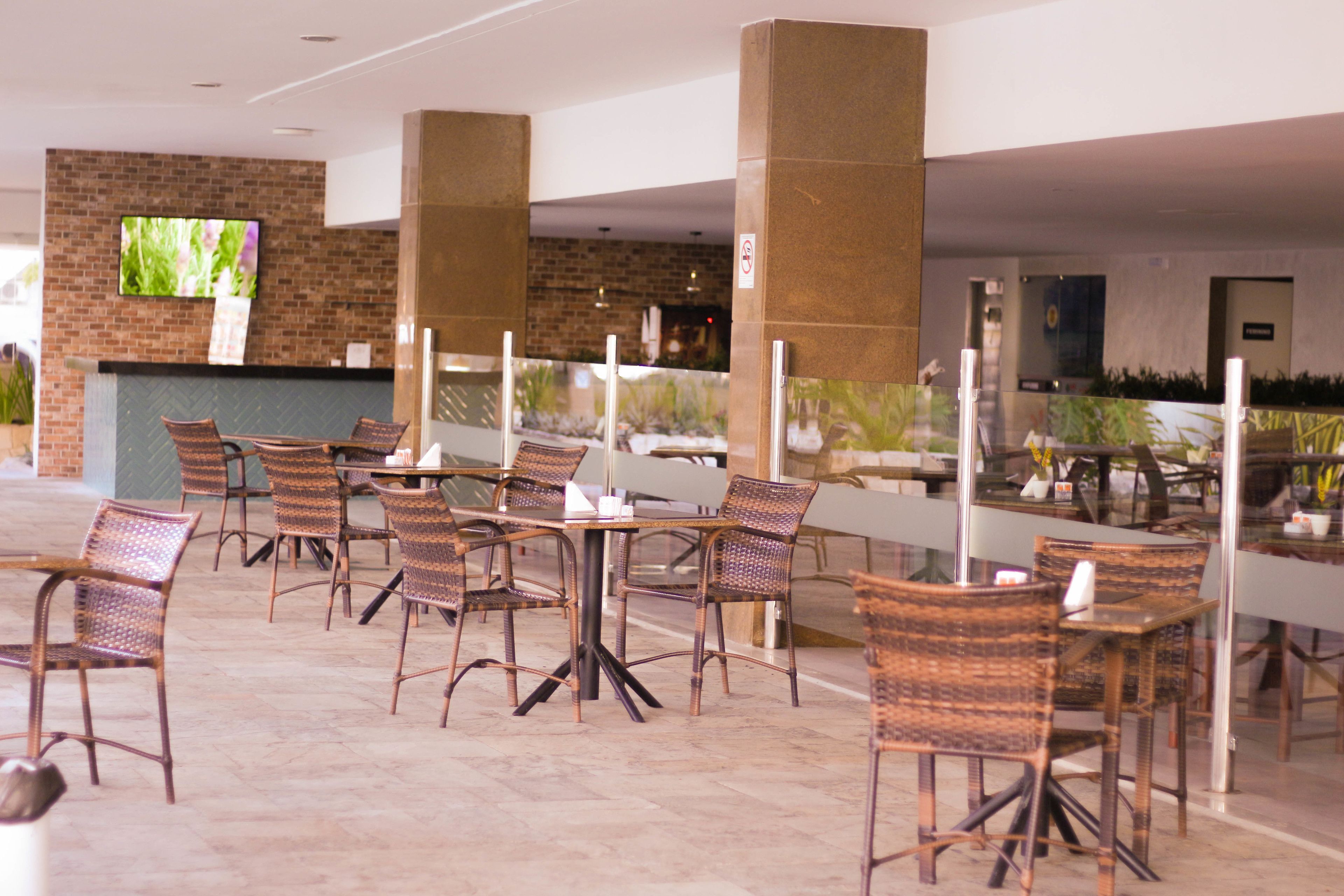 A covered outdoor seating area with wicker chairs and tables, a brick wall with a TV, and a glass partition.
