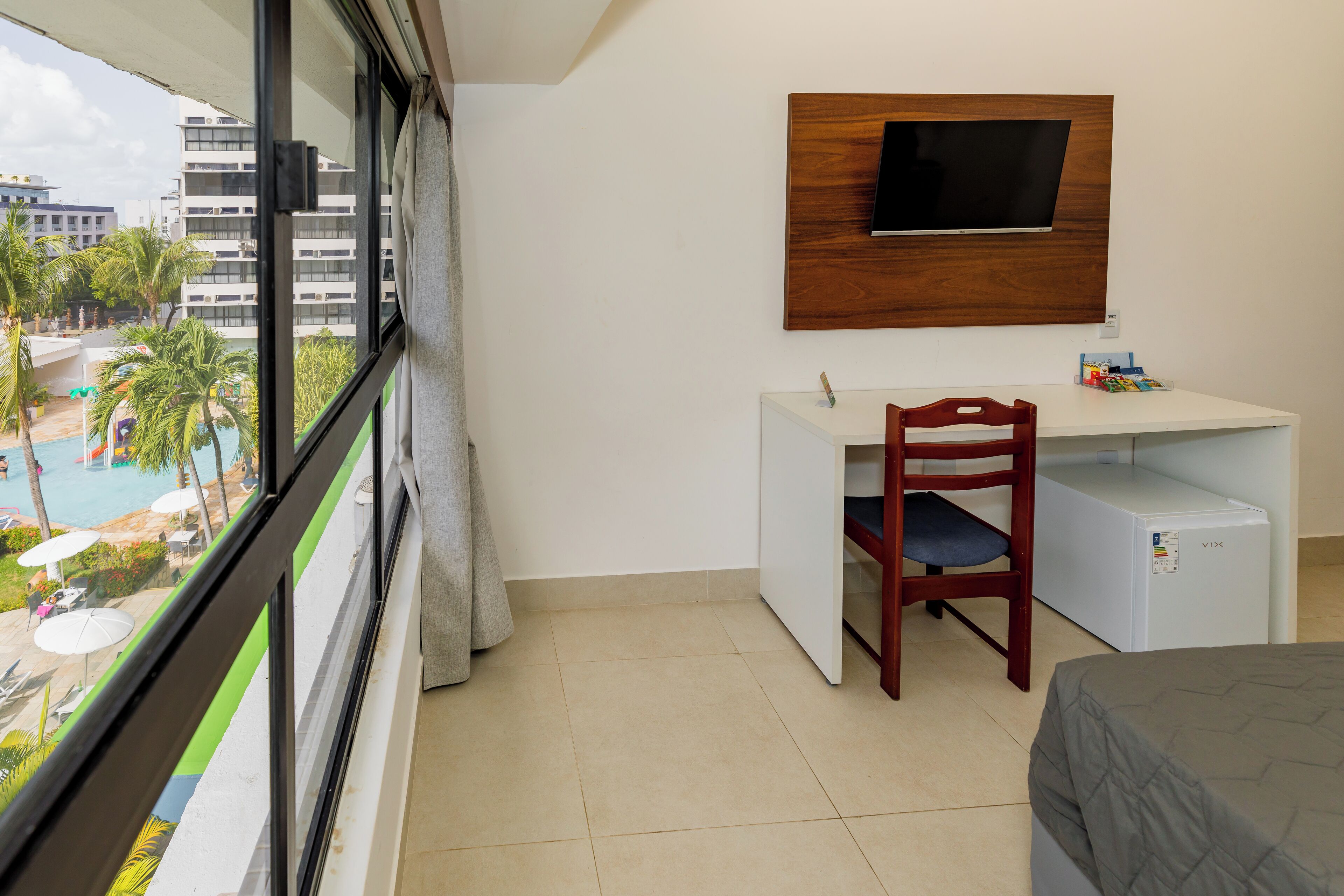 Una camera d'albergo con balcone, una scrivania, una sedia, una TV a muro e un letto.