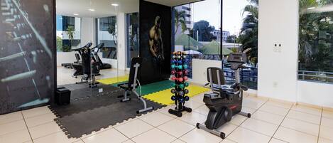 A gym with exercise equipment, a mirror wall, and large windows with a view of palm trees.