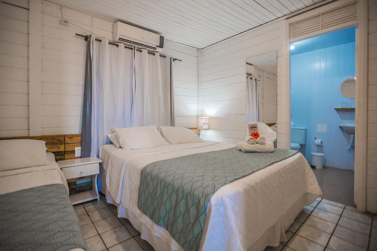 Quarto com duas camas, banheiro com parede azul e teto branco.