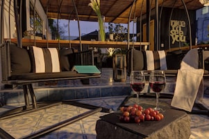 A cozy outdoor seating area with a stone table, two glasses of red wine, and a bowl of grapes.