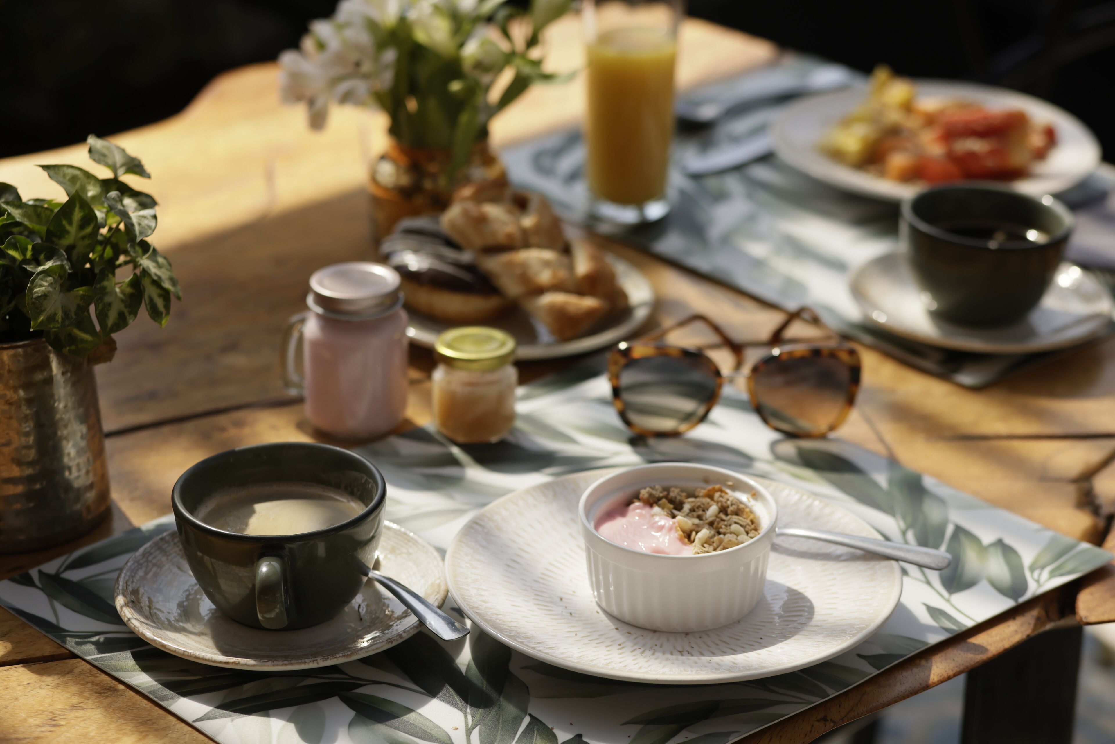 A table with a cup of coffee, a bowl of yogurt, a glass of orange juice, and a plate of food.