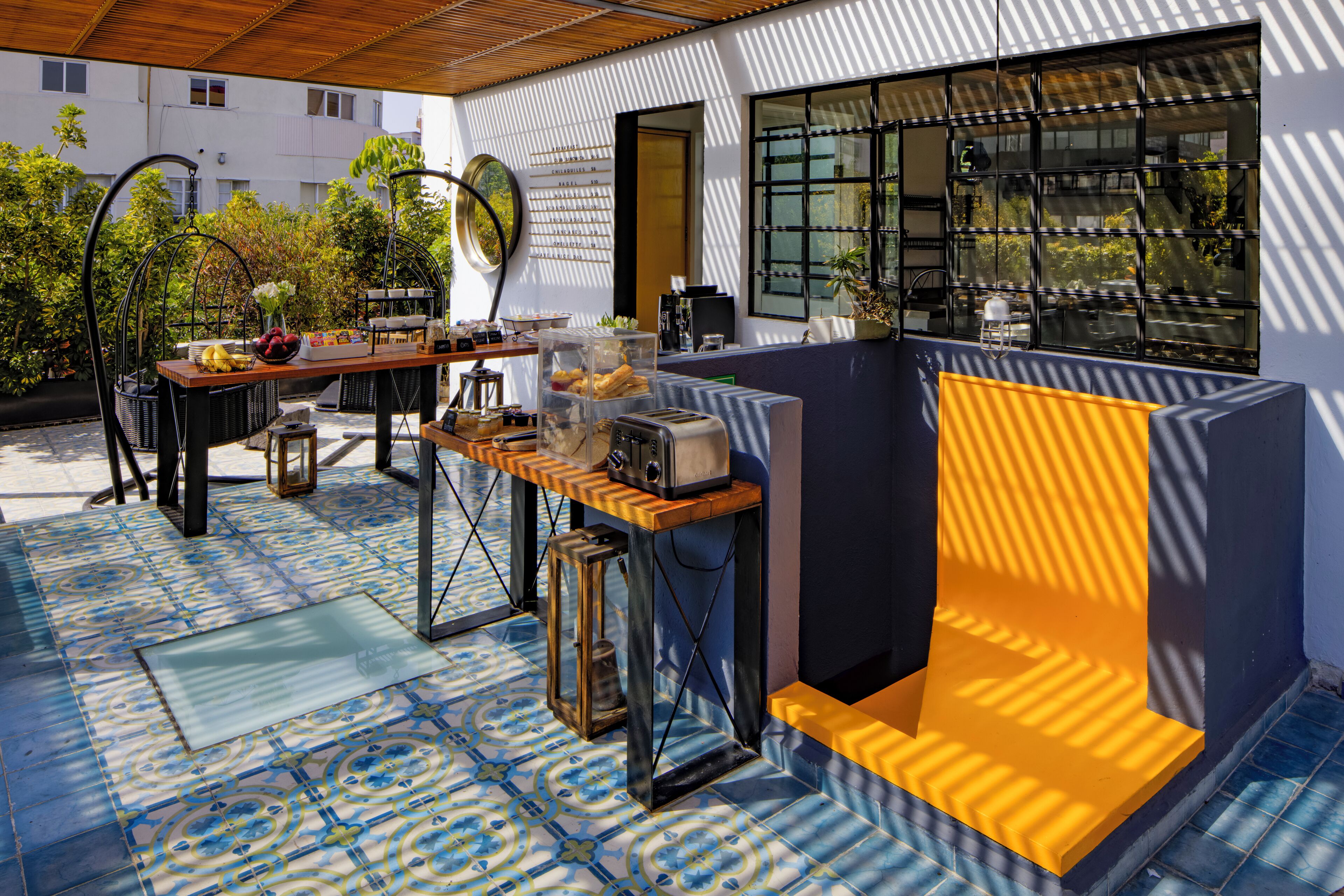 Een terras buiten met een eettafel, stoelen en een zithoek met een geel kussen.