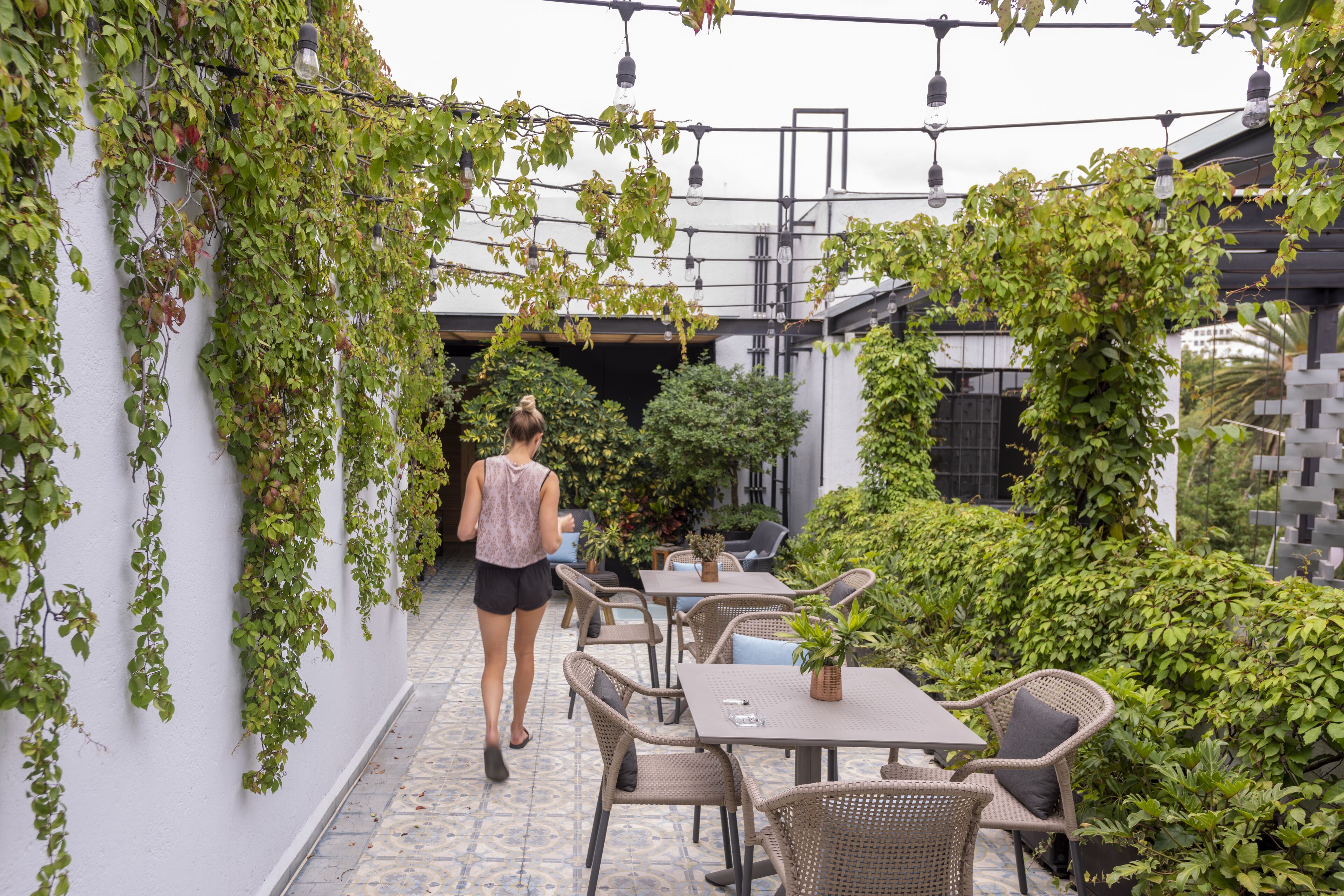 Un'area patio esterna con tavoli e sedie, circondata da vegetazione e piante rampicanti sulle pareti.