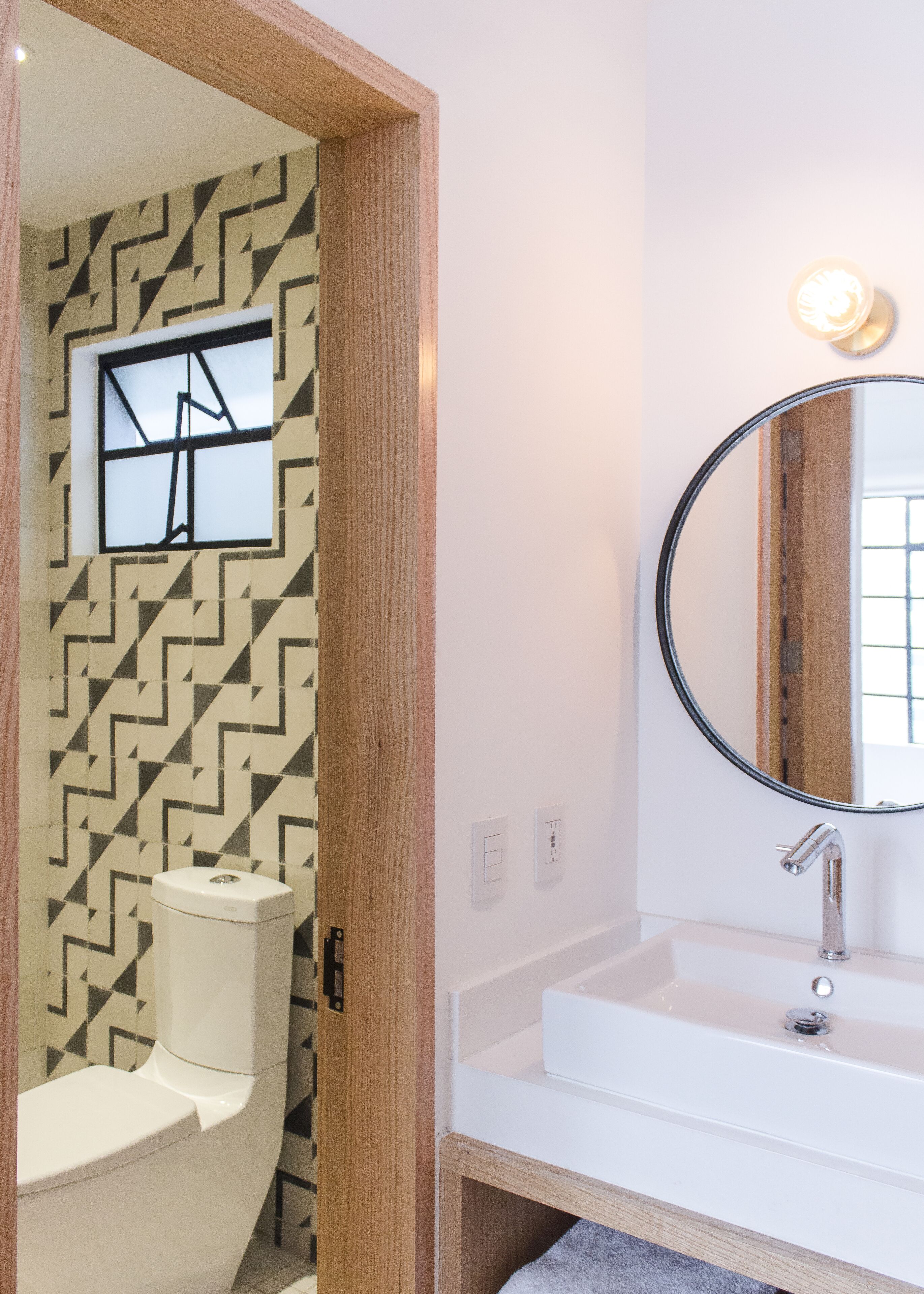 Een moderne badkamer met een wand met geometrisch patroon, een toilet, een wastafel met spiegel en een lamp boven de spiegel.