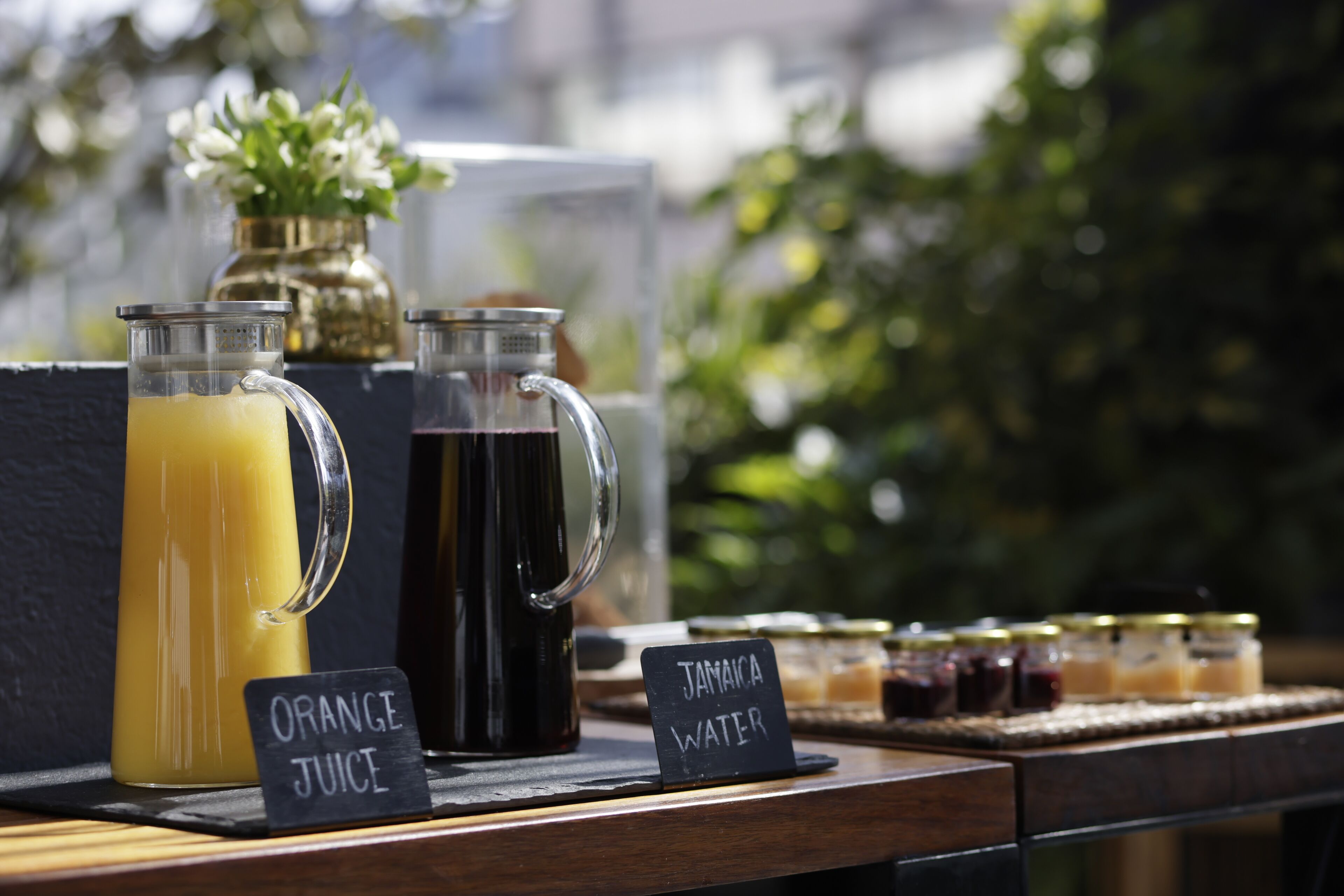 A beverage station with labeled drinks and jars of preserves.