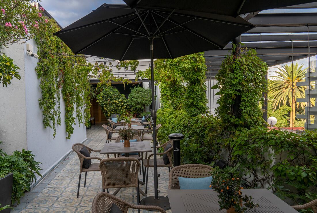 An outdoor patio with wicker furniture, a large umbrella, and lush greenery.