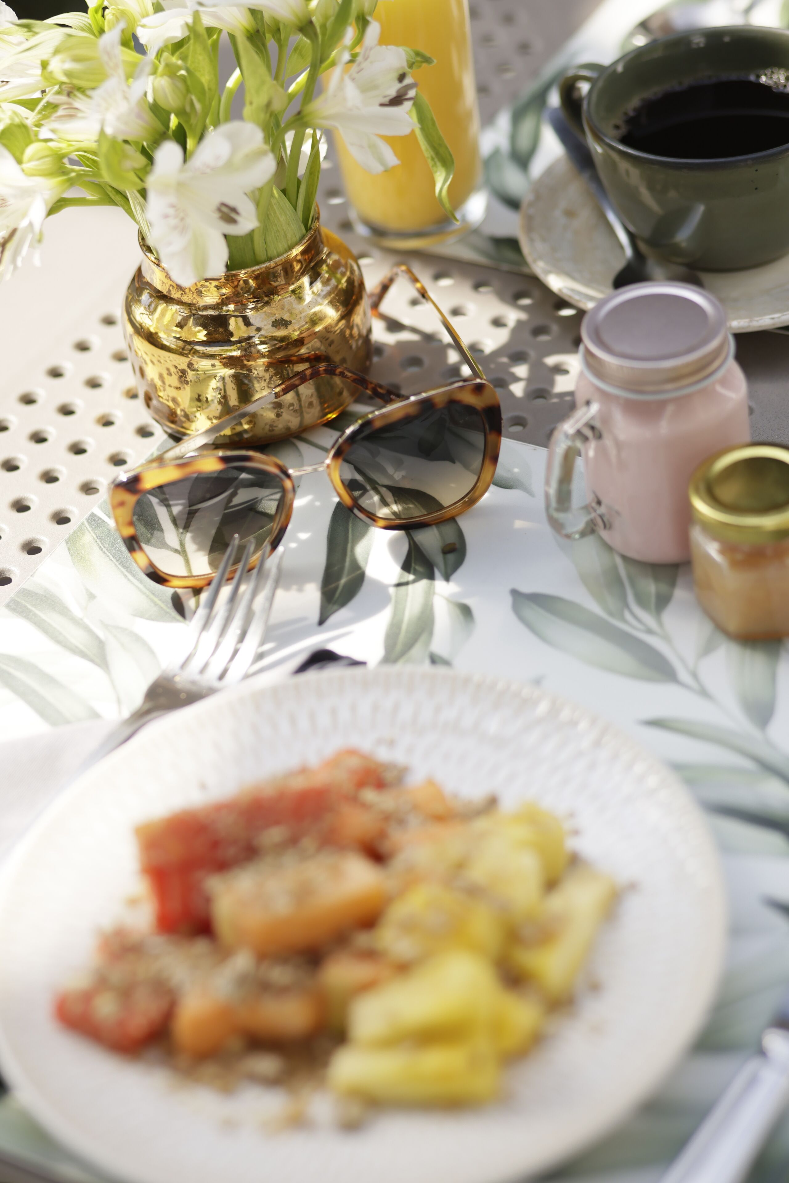 Une table avec une assiette de nourriture, un vase de fleurs, une tasse de café et un pot de confiture.