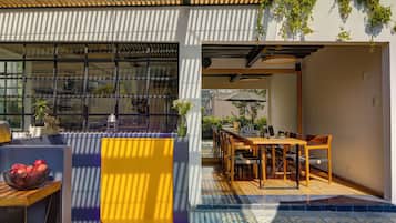 A modern outdoor dining area with a wooden table and chairs, surrounded by potted plants and a blue-tiled floor.