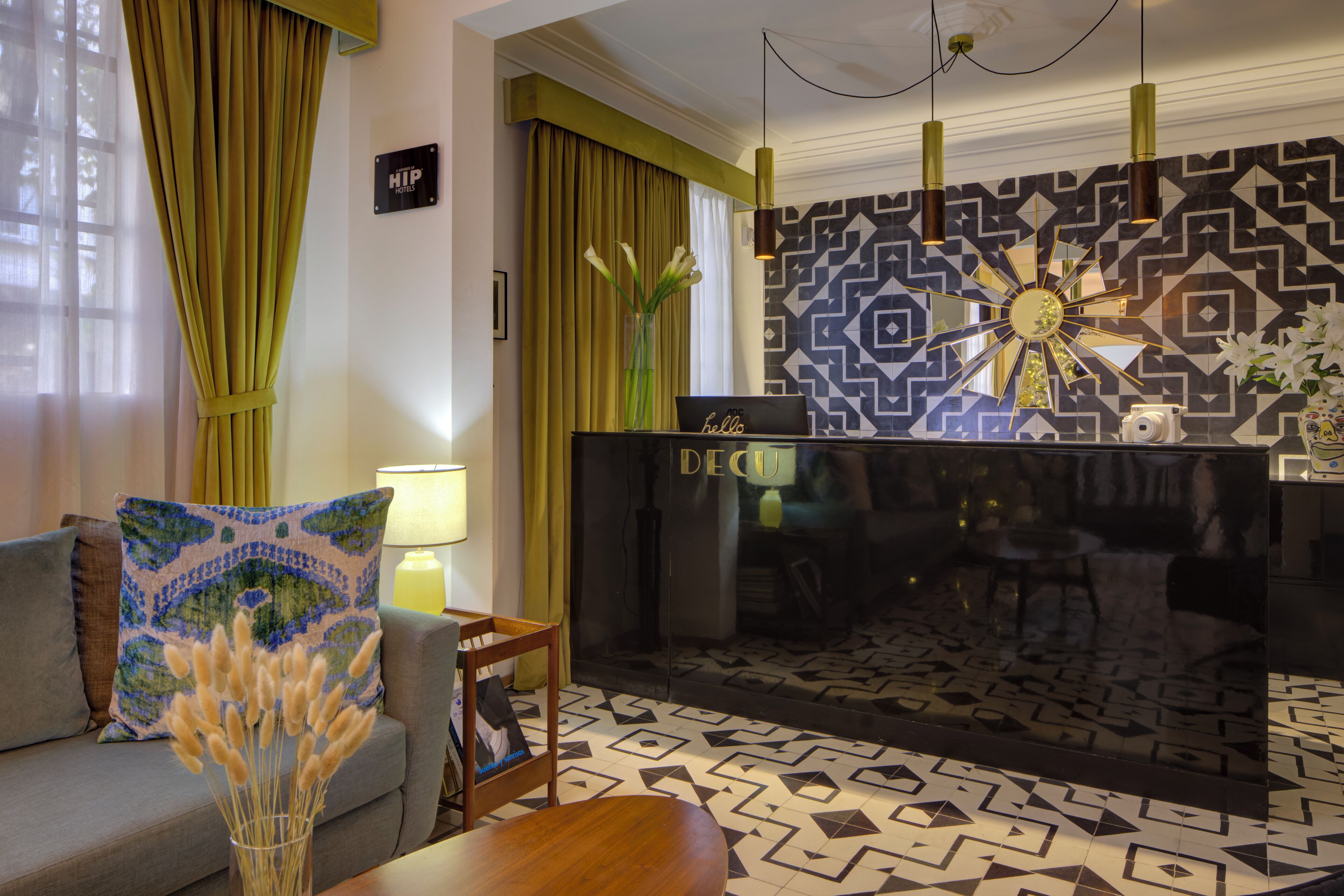 A modern hotel lobby with a sofa, a coffee table, a decorative vase, a fireplace, and patterned tiles on the floor.