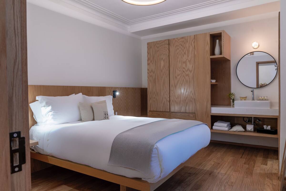 A modern bedroom with a wooden bed, built-in wardrobe, and a round mirror above the vanity.