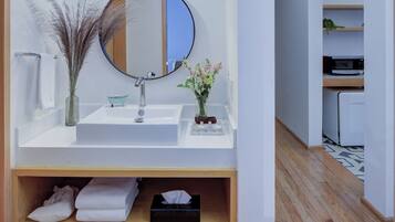 Un baño moderno con un lavamanos blanco, un espejo redondo y una estantería de madera con toallas y una caja de pañuelos.