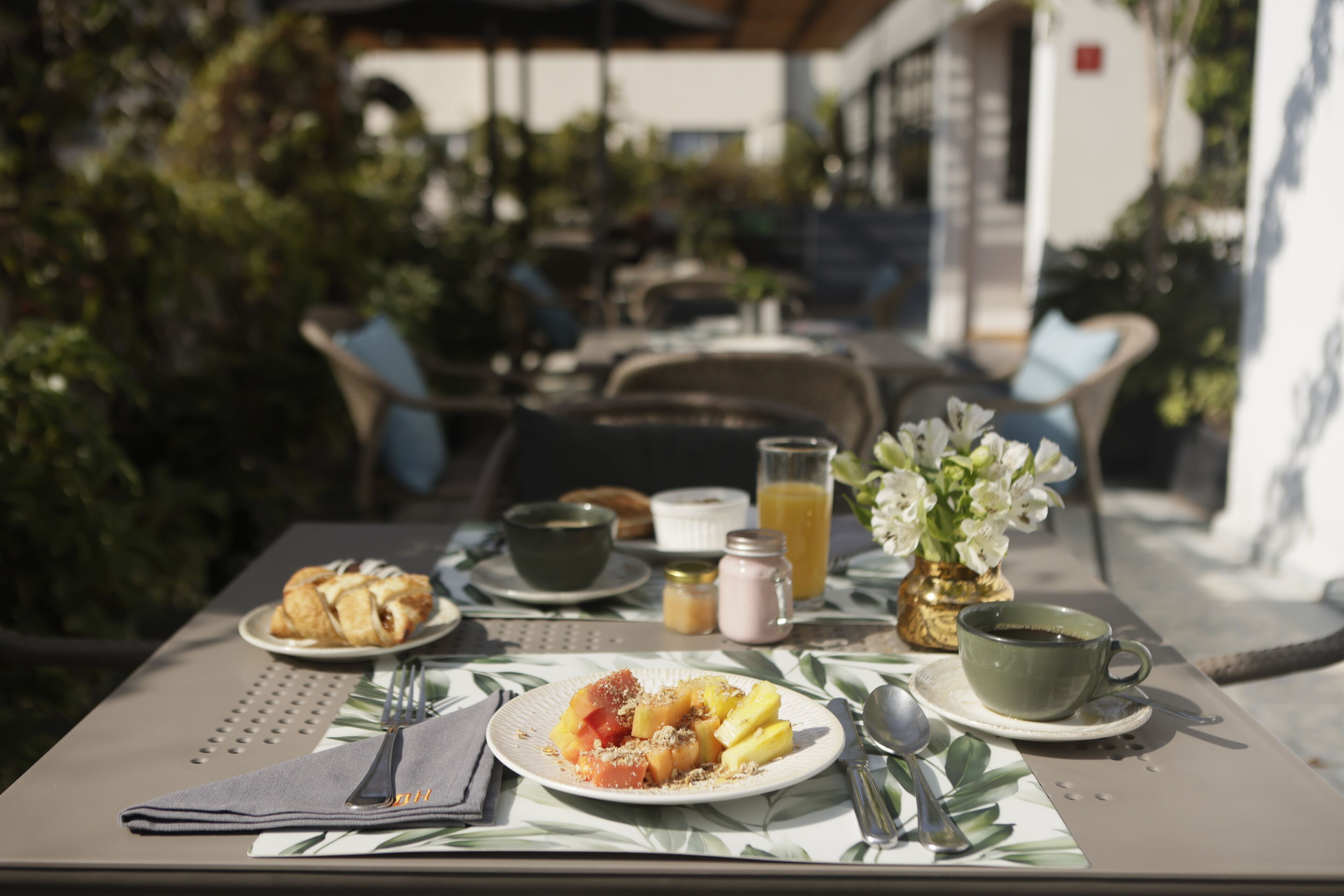 A table set for breakfast with plates of food, a cup of coffee, and a vase of flowers.