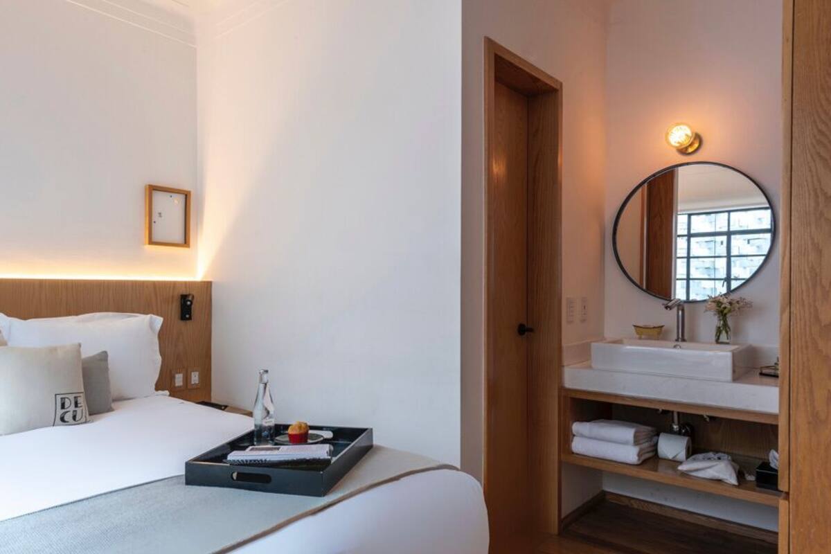 A hotel room with a bed, bedside table, and a bathroom with a mirror and sink.