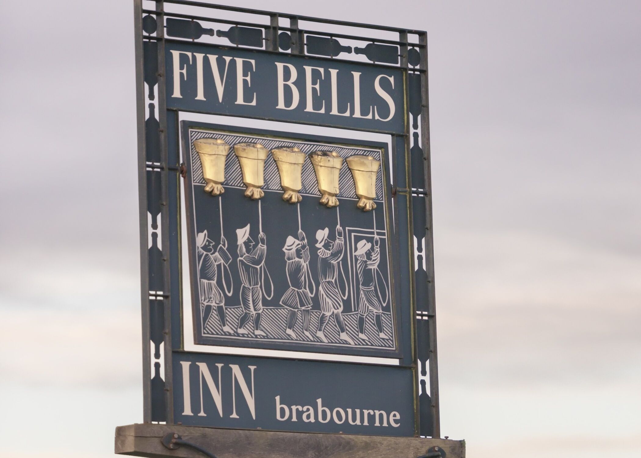 Señal del Five Bells Inn en Braburne, con un diseño tradicional que muestra una hilera de figuras de campanas y una representación de personas.