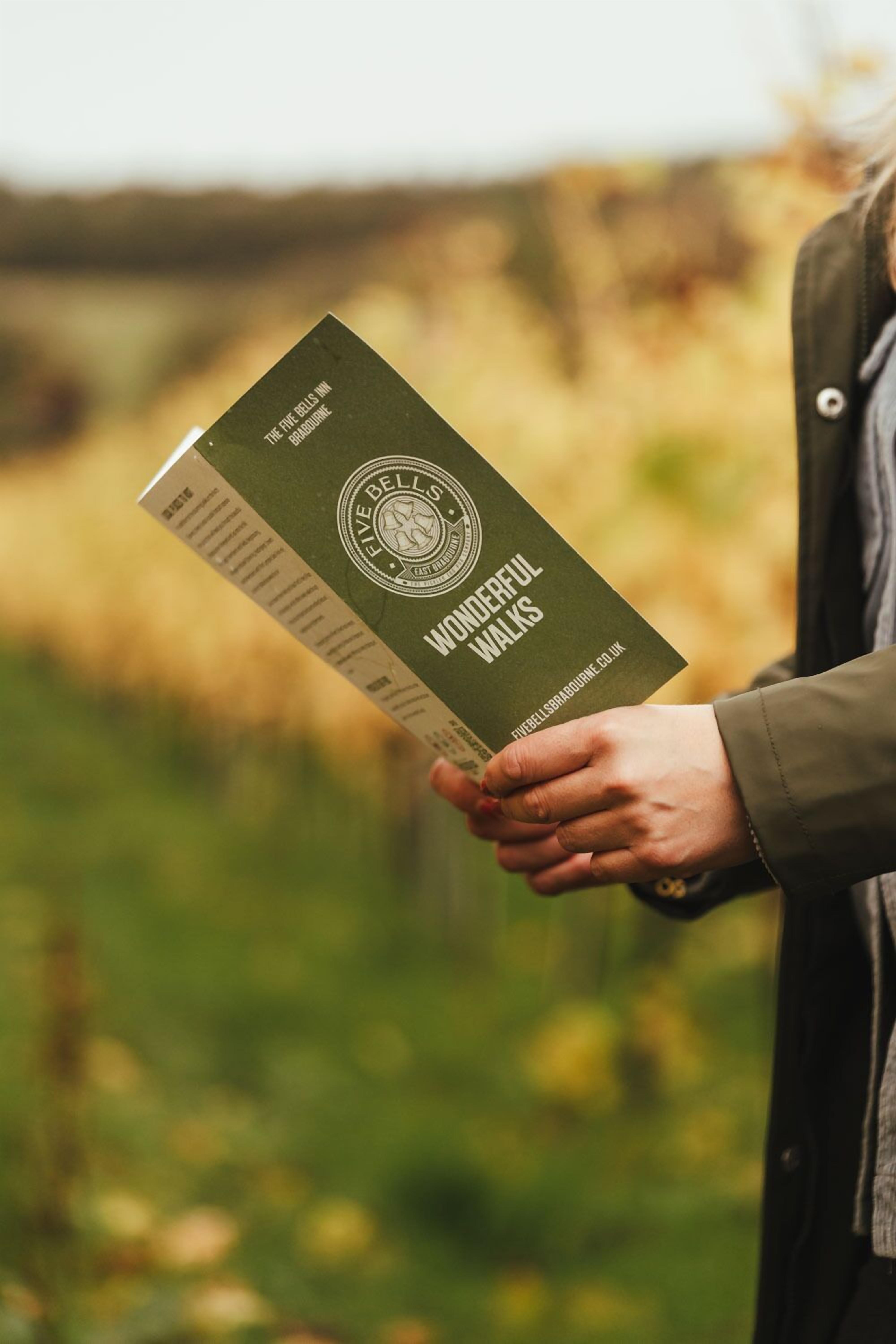 A person holding a booklet titled "The Five Bells Inn Wonderful Walks."