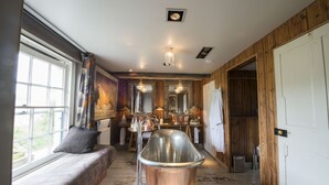 A rustic interior with a large bathtub, wooden walls, a bench with cushions, and a dining area with a chandelier. - The Five Bells Inn Brabourne (Ashford)