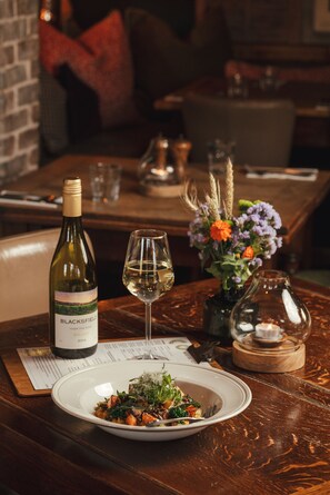 A dining table with a bottle of wine, a glass of wine, a plate of food, and a vase with flowers. - The Five Bells Inn Brabourne (Ashford)