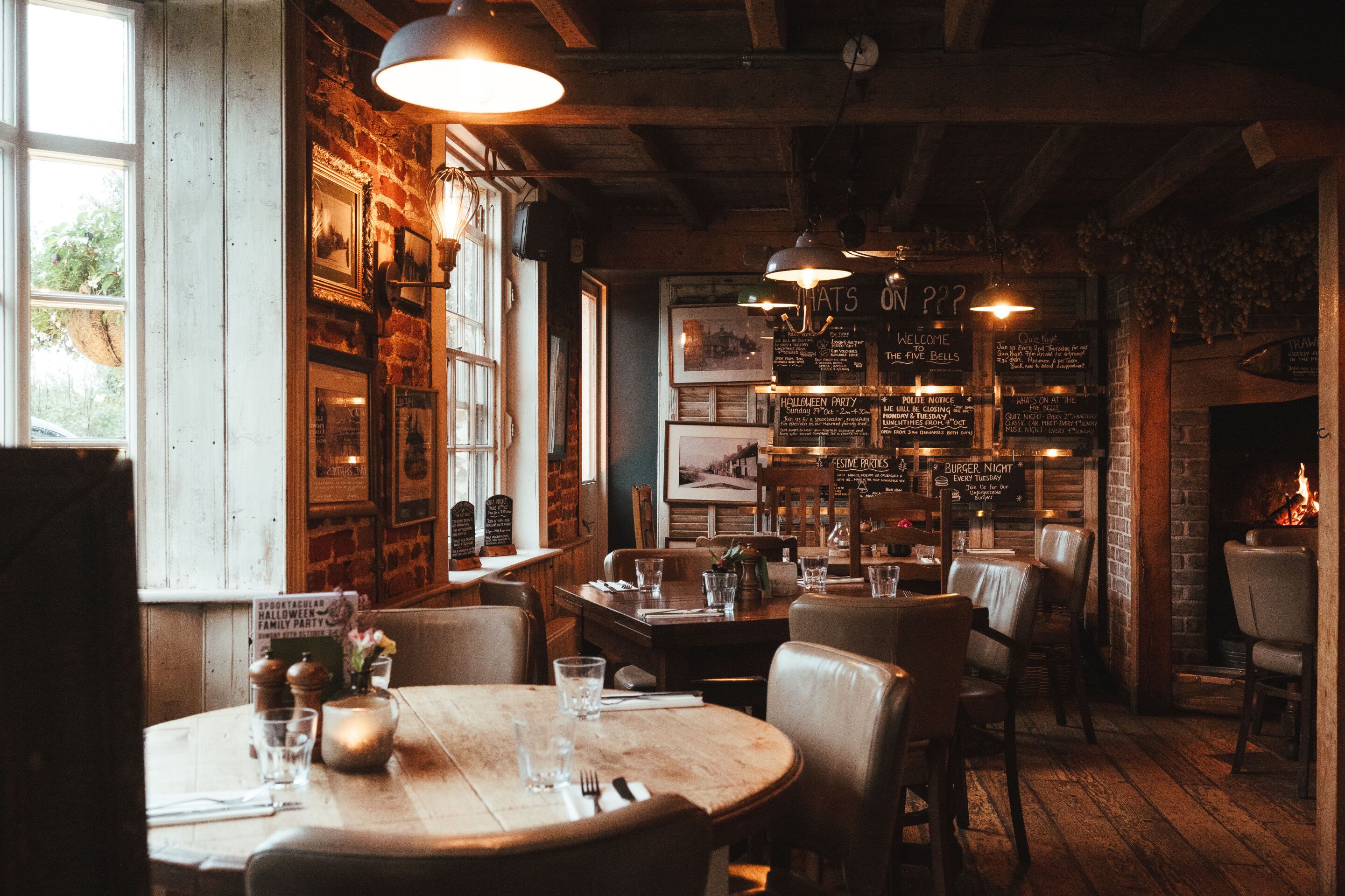 A cozy restaurant with brick walls, wooden tables, and hanging lights.