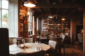 A cozy restaurant with brick walls, wooden tables, and hanging lights. - The Five Bells Inn Brabourne (Ashford)