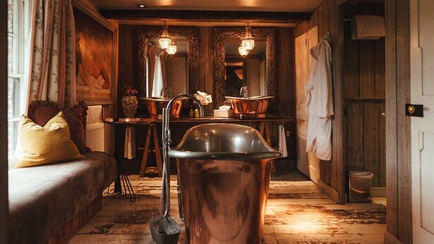 A rustic bathroom with a large copper sink, wooden vanity, and a chandelier. - The Five Bells Inn Brabourne (Ashford)