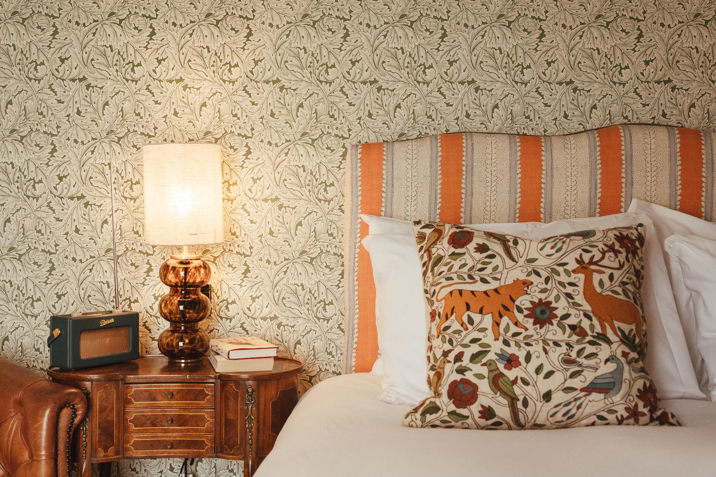 A neatly made bed with a patterned pillow, a bedside lamp, and a small wooden nightstand with a book and a radio.