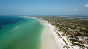 An aerial view of a beach resort with a long sandy beach, clear turquoise waters, and thatched-roof buildings. - La Casa del Alux - Adults Only (Isla Holbox)