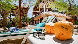 A beachside lounge with striped cushions, a thatched-roof structure, and a large orange fruit in the foreground. - La Casa del Alux - Adults Only (Isla Holbox)