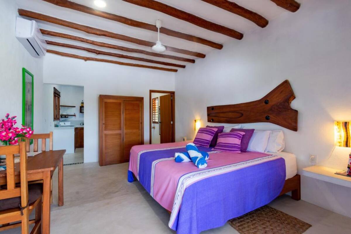 Un dormitorio con dos camas, vigas de madera en el techo, un escritorio con silla, y una mesita de noche con lámpara.