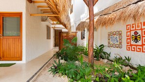 A narrow pathway with a thatched roof structure, surrounded by tropical plants and a decorative wall with geometric patterns. - La Casa del Alux - Adults Only (Isla Holbox)