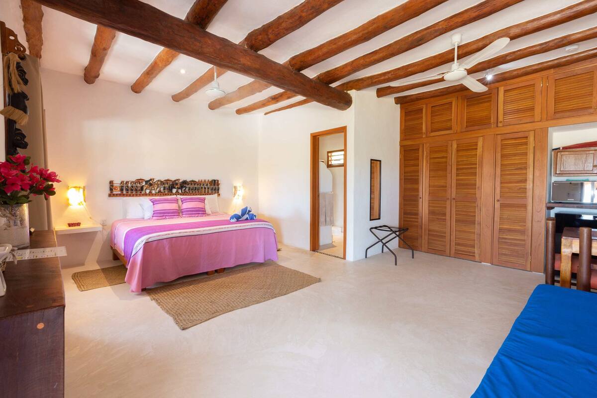 Un dormitorio con cama, vigas de madera en el techo, un ventilador de techo y un armario.