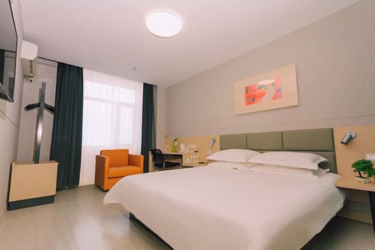 Une chambre d’hôtel avec un lit, un bureau, une chaise, une petite table avec une plante et un tableau au mur.