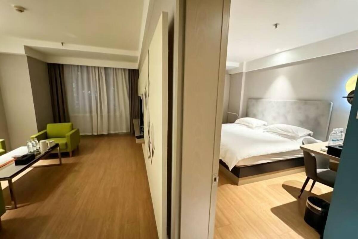 A hotel room with a bed, a desk, a chair, a green sofa, and a curtain.