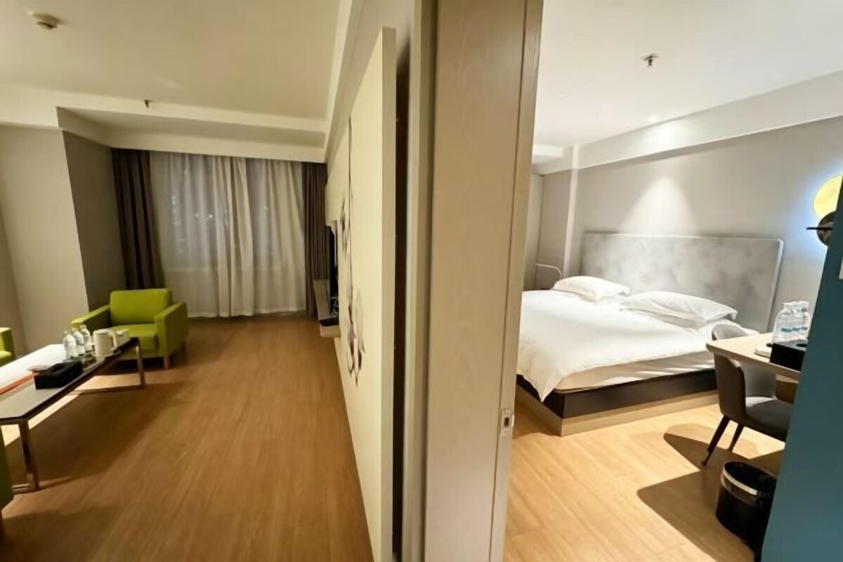 A hotel room with a bed, a desk, a chair, a green sofa, and a curtain.