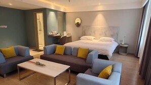 Moderni hotellihuone, jossa on sänky, kaksi sohvaa, sohvapöytä, työpöytä ja suihkutila.
