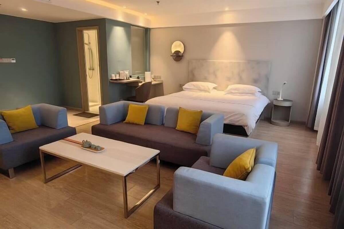 A modern hotel room with a bed, two sofas, a coffee table, a desk, and a shower area.