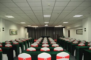 Un salón de conferencias con filas de mesas, cada una con mantel verde y funda para silla con estampado blanco y rojo.