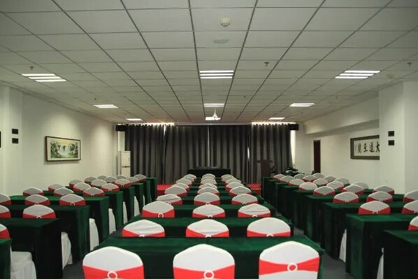 Une salle de conférence avec des rangées de tables, chacune recouverte d’une nappe verte et agrémentée d’une housse de chaise blanche et rouge à motifs.