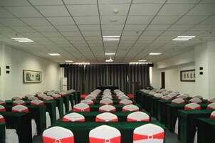 Un salón de conferencias con filas de mesas, cada una con mantel verde y funda para silla con estampado blanco y rojo.